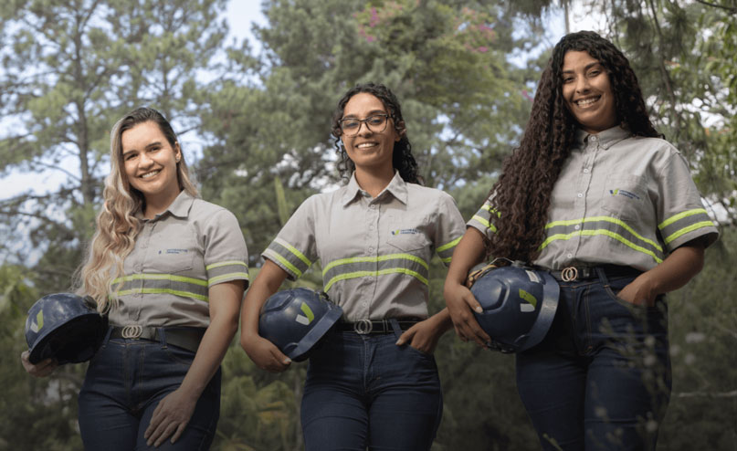 three women pose side by side holding hard hats